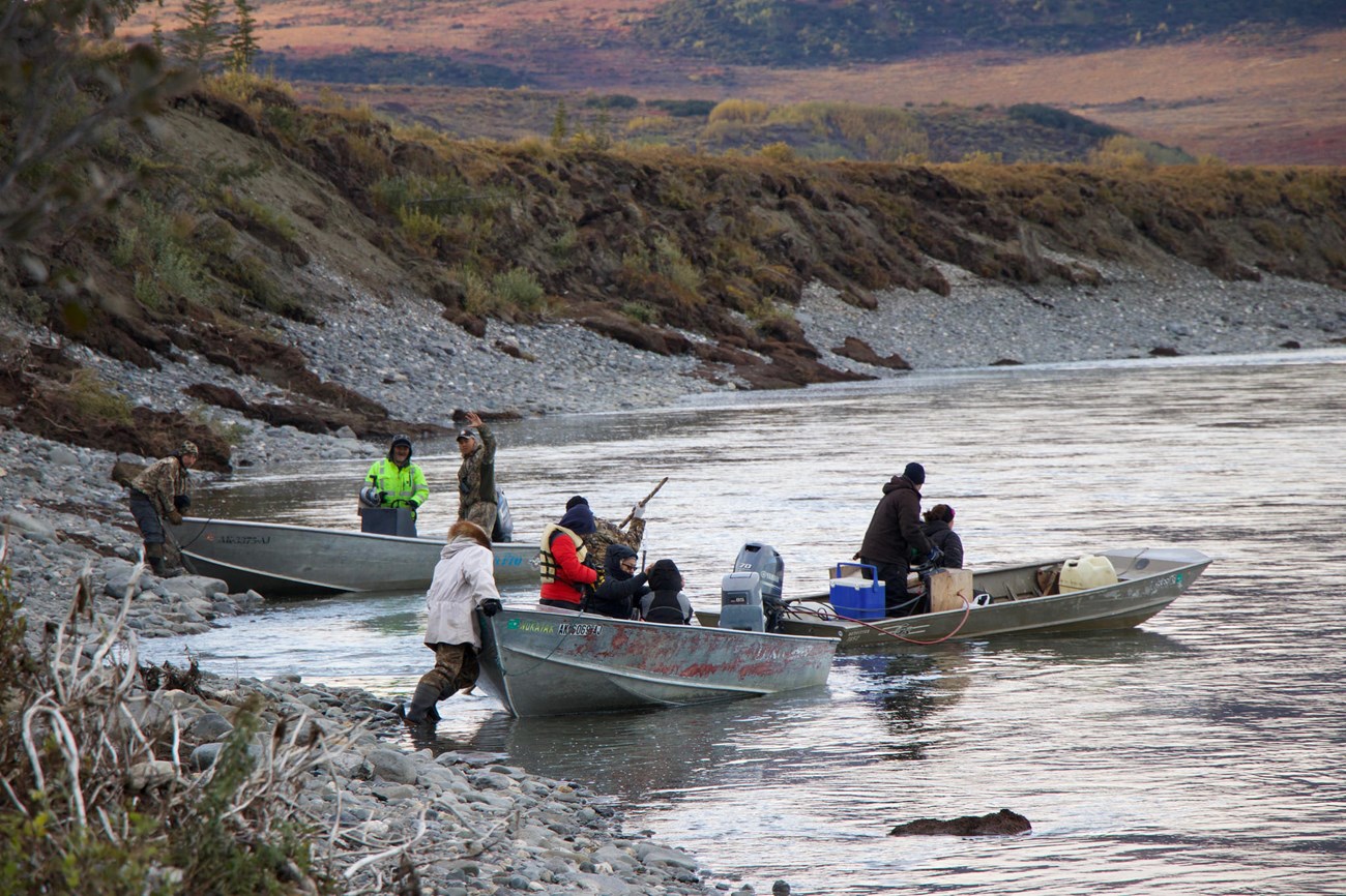 People push off from shore of a river in three small metal boats.