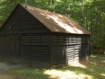Dappled sunlight on a wooden bathhouse with rough siding and a door on one side.