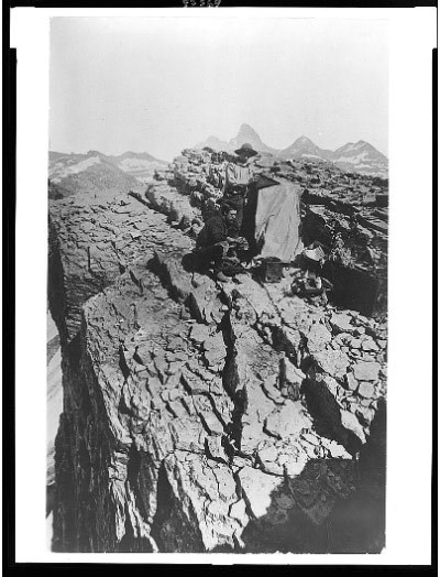 lt= Two men stand with camera equipment on a rocky mountaintop.