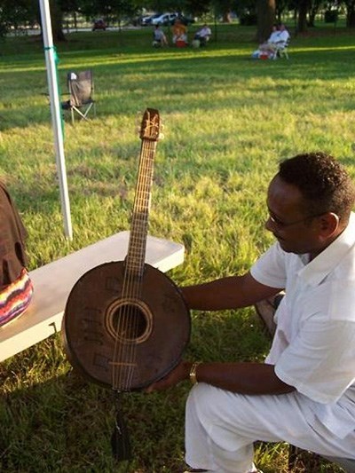 A seated man looks down at a round-bodied guitar he holds in both hands.