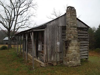 A log house with a stone foundation and stone chimney in a rural landscape.