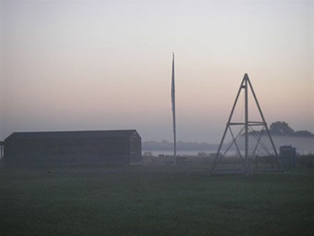 Pyramid shaped catapult in an open field, dimly lit and bathed in fog.
