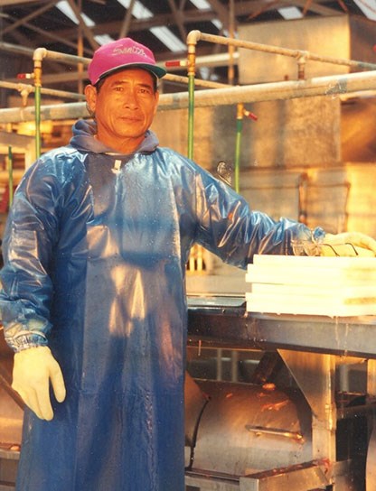 A man with waterproof smock and rubber gloves, standing inside a warehouse, looks at the camera