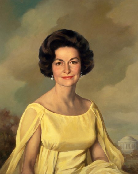 A portrait of Lady Bird Johnson with short brown hair and a delicate yellow dress.