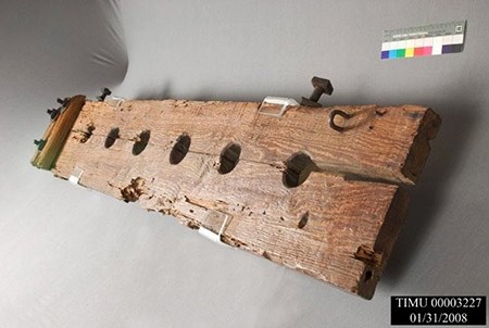 Shackles, circa 1810-1835 A long wooden board has a split down the middle and an evenly-spaced row of round holes.