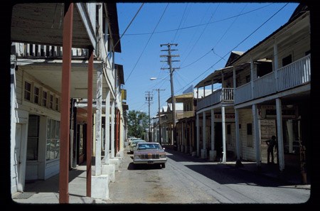 A street is lined by two rows of houses with second-story porches and wood railings.