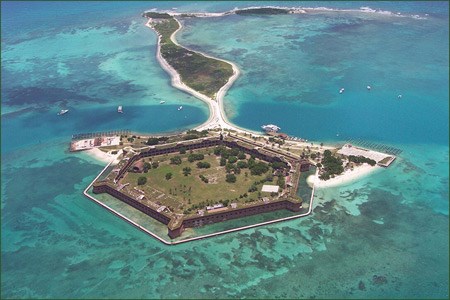 Bright blue-green water surrounds a fort, its walls surrounding open lawn.