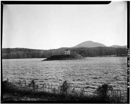 A gazebo-like structure stands on a knob of land in a grassy field.