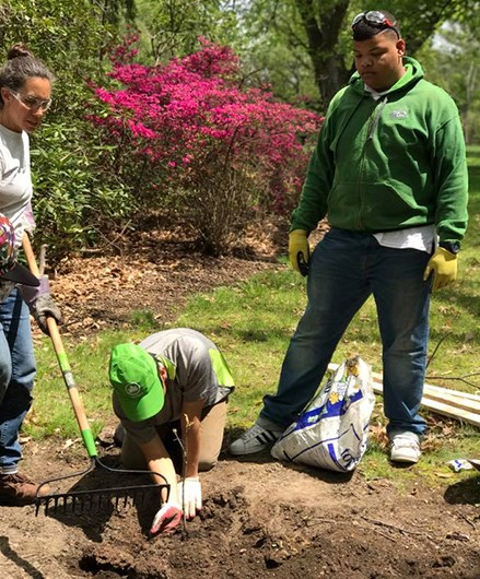 Three students plant a young tree in overturned soil