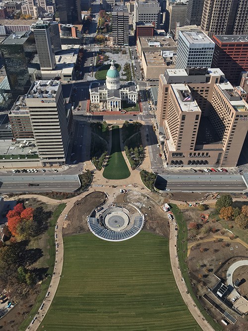 View of the Gateway Arch landscape from above includes a walkway curving around turf, construction, and a courthouse surrounded by downtown St. Louis.