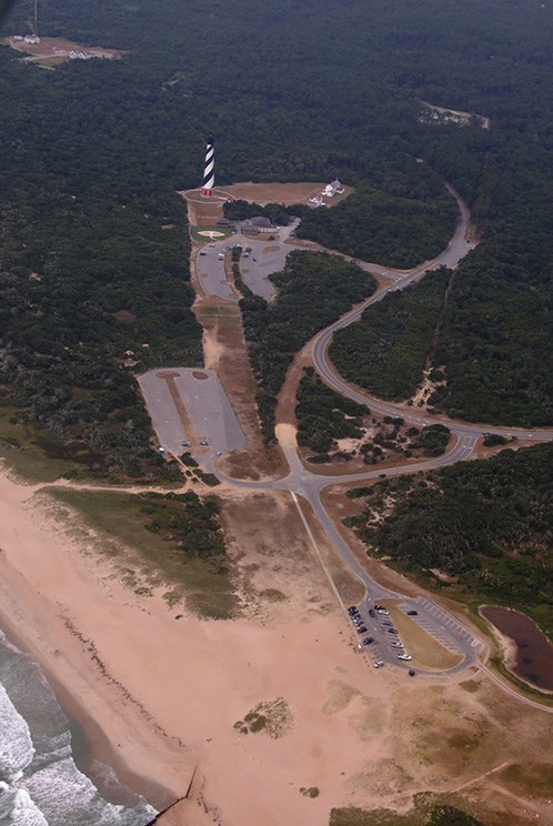 Aerial view of the striped Cape Hatteras lighthouse at the end of a long clearing from the shoreline.