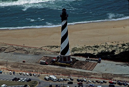 Cape Hatteras light tower is moved along a wide path between a beach and a parking lot.