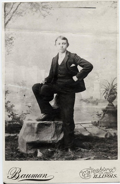 A young Carl Sandburg in a three-piece suit poses for a photo, one foot raised on a rock.