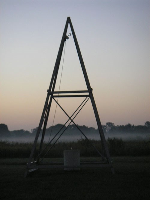500-DAAV-catapult Wooden catapult structure shaped like a tall pyramid stands in a hazy field at dawn