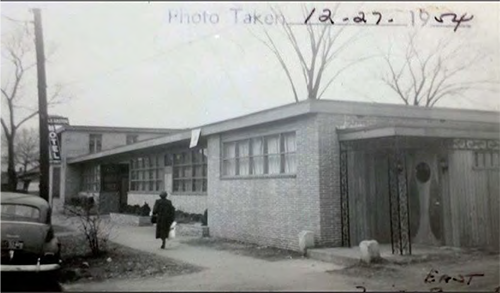 A person walks on a sidewalk beside the facade of Gaston Motel in 1954, lined with blocks of windows