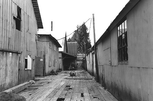 Wooden warehouse buildings line both sides of a wooden boardwalk