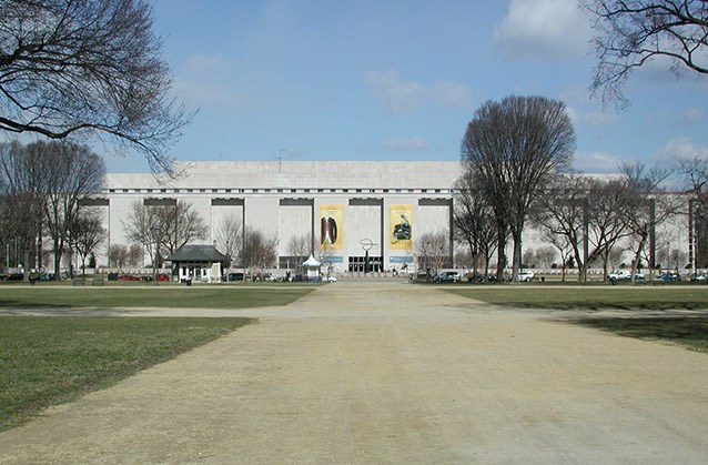 View of the National Museum of American History following 13th Street View of the National Museum of American History following 13th Street, with elms arising in the foreground of the building on either side of the broad walkway leading to its doors.