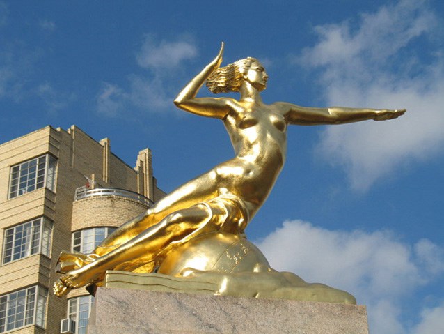 The dynamic, gilded bronze form of a woman with her left arm outstretched and her hair blowing behind her.
