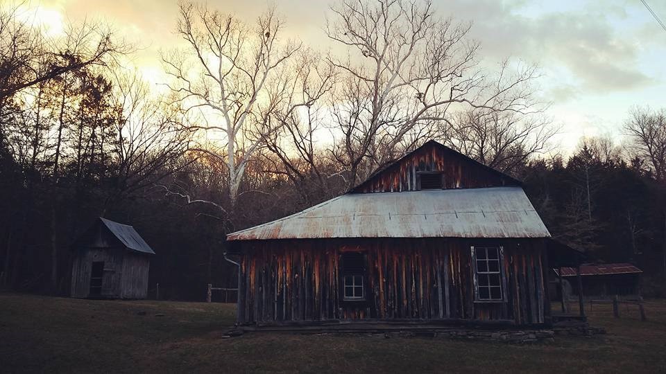 A two-story log structure with several outbuildings at sunset