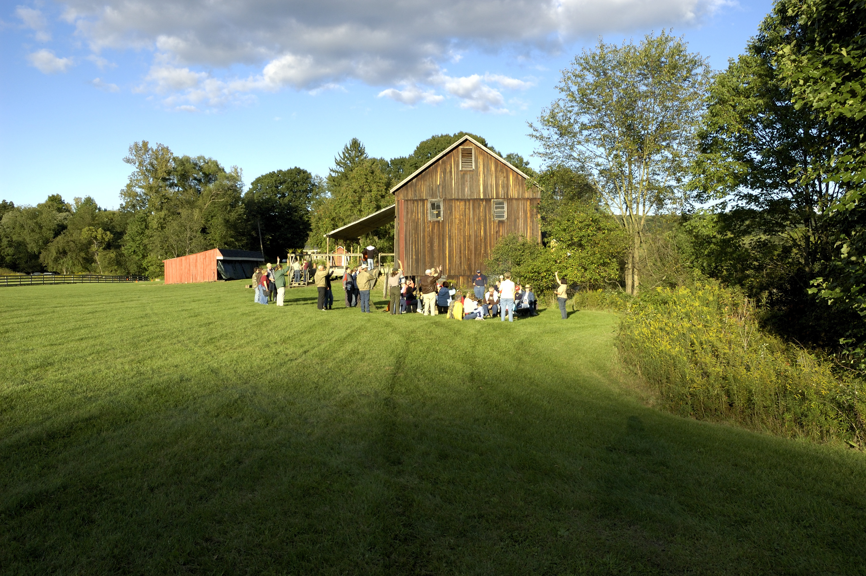 A group of people stands in mowed grassy area beside a large barn