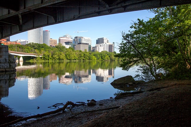 A view from the shade below a bridge across the sunny, calm Potomac River