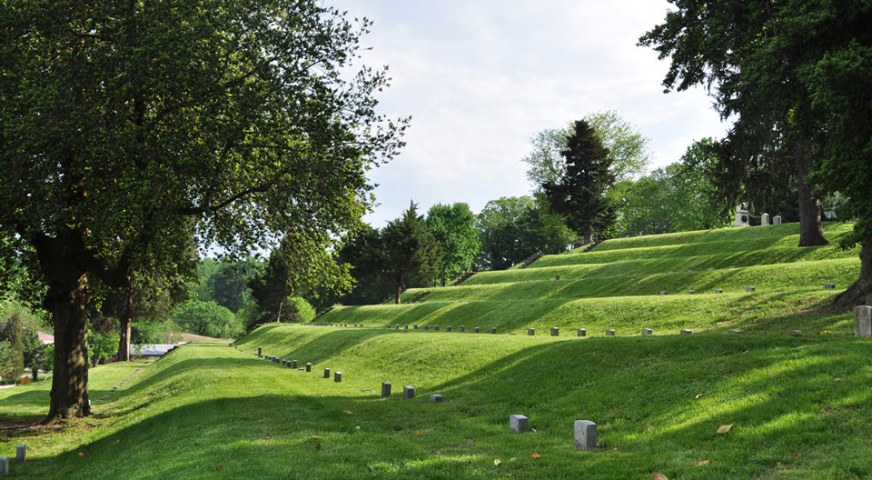 Headstones line up in low rows on terraced earthworks.