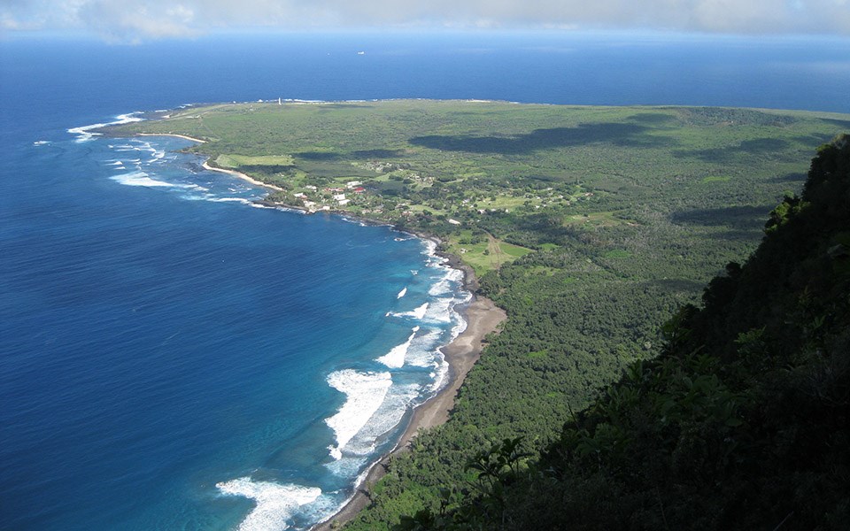 View from the Pali Trail to Kalaupapa Peninsula, level and green surrounded by bright water.