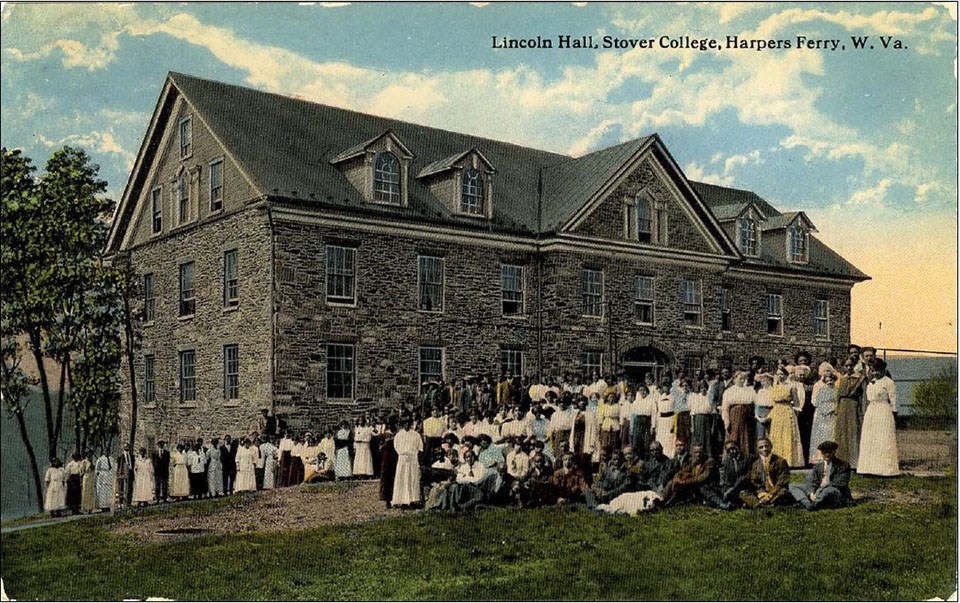 A tinted postcard shows a group of students and instructors, many African American, in front of the large stone Lincoln Hall at Storer College
