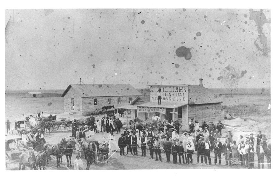 Historic photo of the town of Nicodemus with many people and horses in front of a few structures.