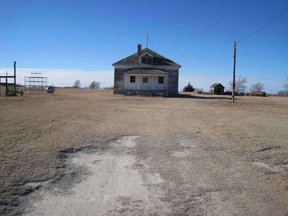 Nicodemus School District 1 A wooden schoolhouse stands on flat, open land surrounded by a jungle gym and short grass.