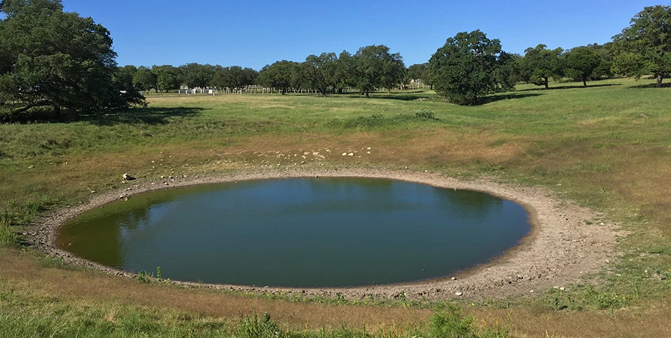 Water Tank at LBJ Ranch A still, round water pool is surrounded by a gently-rolling agricultural landscape.