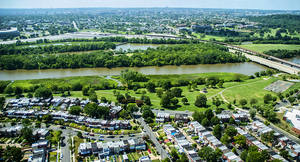 Aerial view of green space along a river, through the middle of a neighborhood and highways.