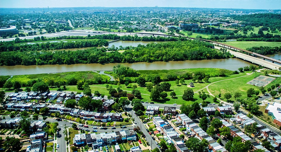 Aerial view of green space along a river, through the middle of a neighborhood and highways.