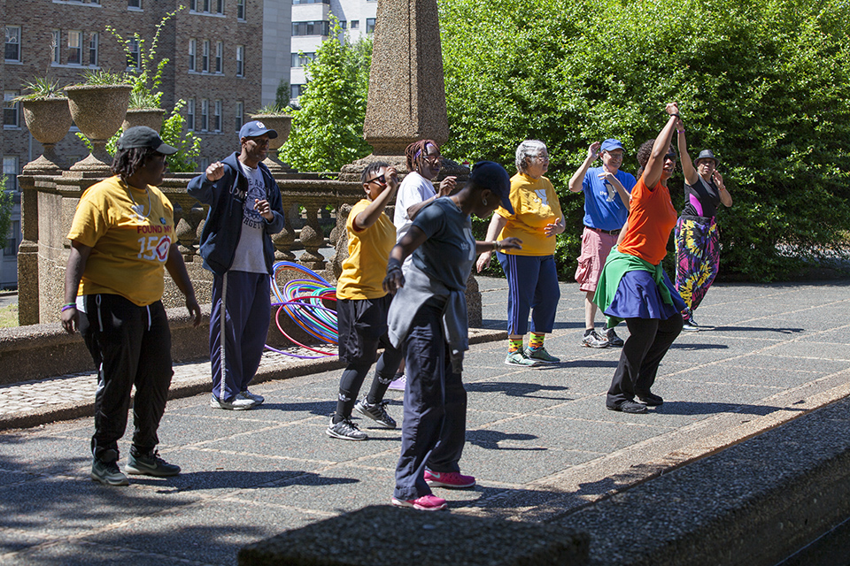 Individuals of varying ages do Zumba on a paved area at Meridian Hill Park.