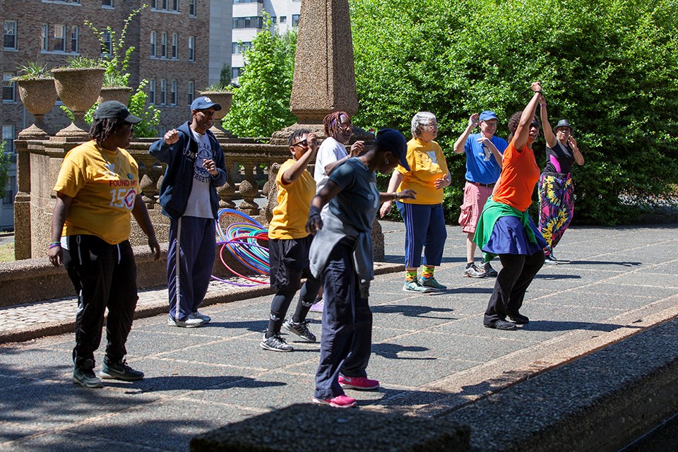 Individuals of varying ages do Zumba on a paved area at Meridian Hill Park.