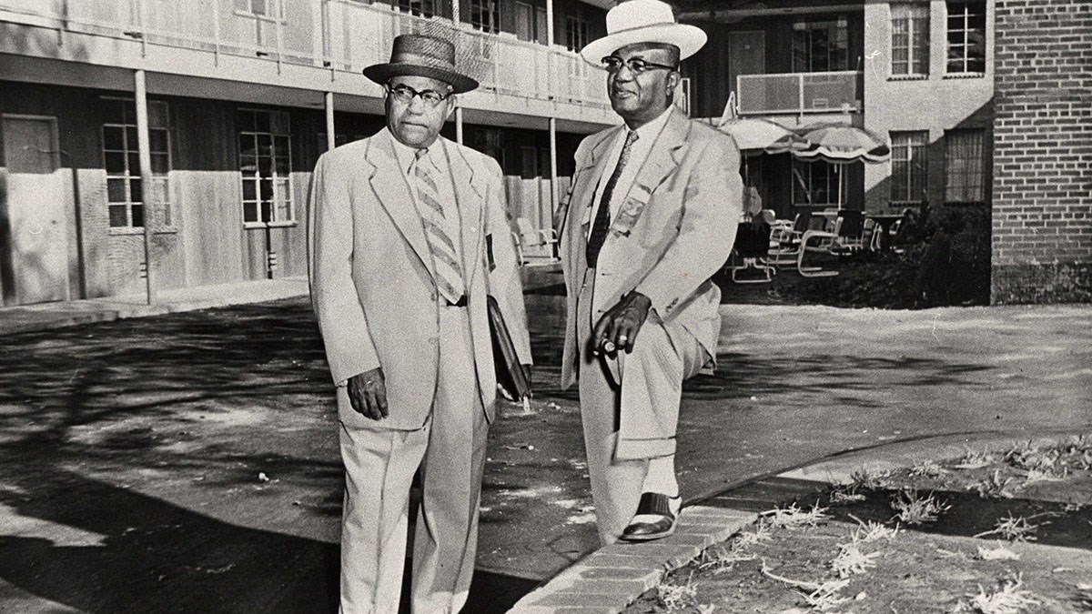 A.G. Gaston and R.A. Hester stand in a motel courtyard, wearing suits, ties, and brimmed hats