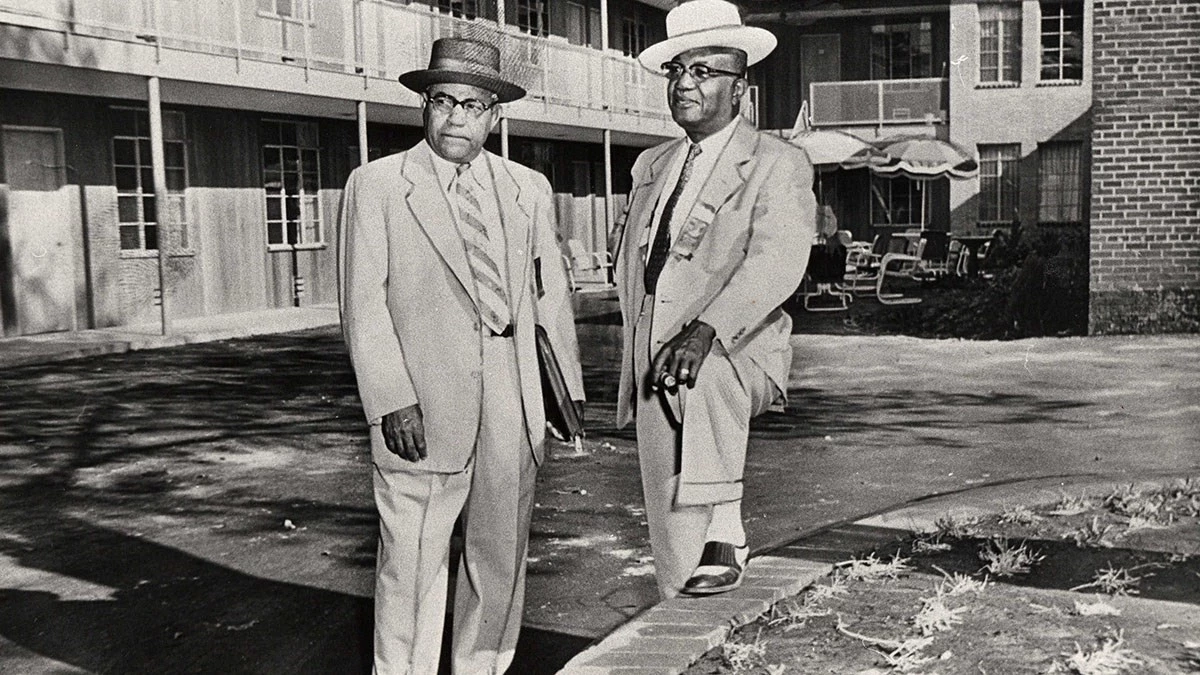 AGGaston-RAHester_Birmingham-Archives A.G. Gaston and R.A. Hester stand in a motel courtyard, wearing suits, ties, and brimmed hats