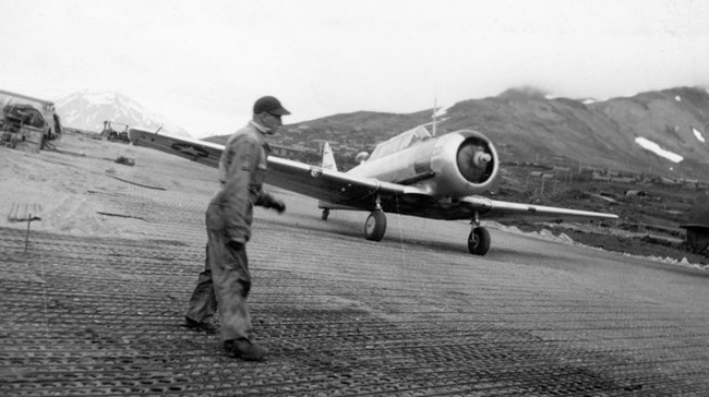MSgt Nelson and AT-6 A man in coveralls stands on an airfield in front of a small plane