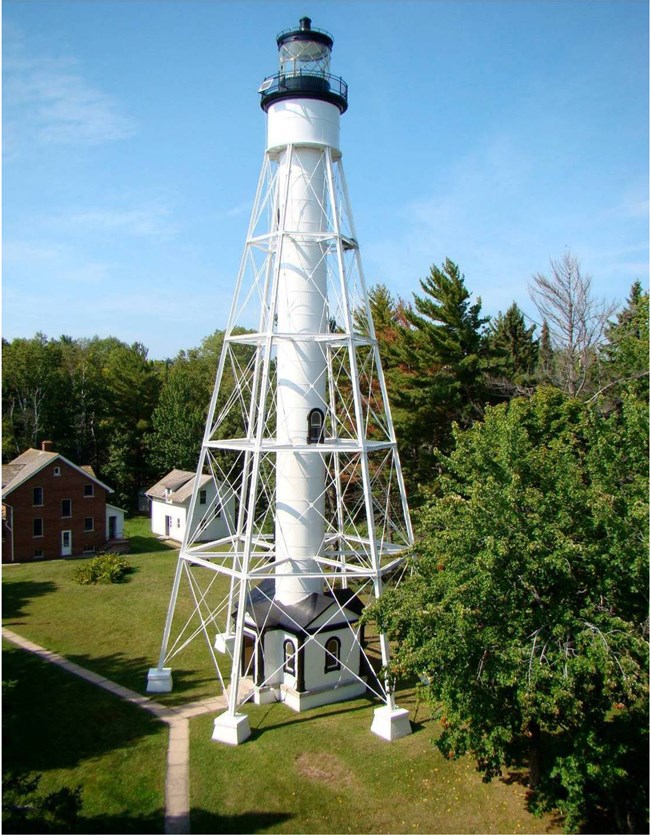 APIS-Michigan-Light-CLR-HSR A tall light house with a beacon standing on metal legs, surrounded by a clearing of lawn and pathways