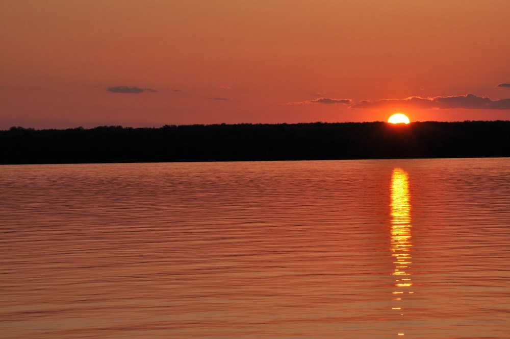 Glowing sun dips under the horizon, turning the sky orange and reflecting in the water of Lake Superior.