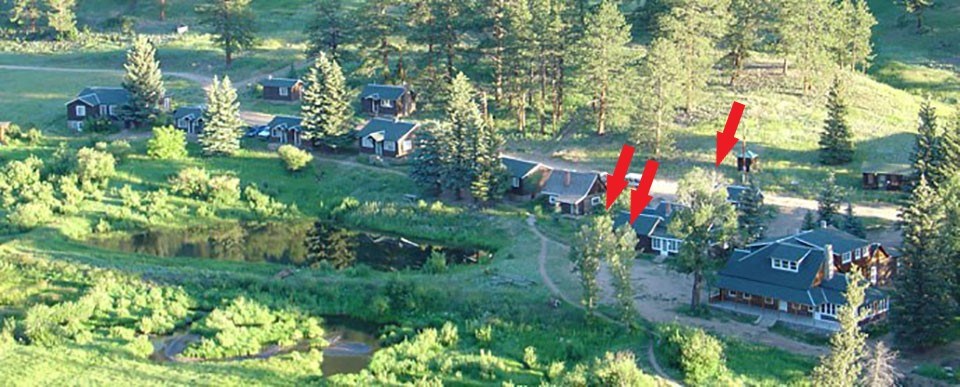Aerial view of ranch with a row of cabins and buildings, pond, scattered trees, and pathways