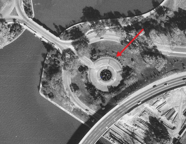 Aerial view of a round fountain and surrounding garden, shrubs, and trees. An arrow points to a ring of forsythia around the fountain.