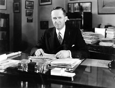 A man in a suit and tie sits behind a desk