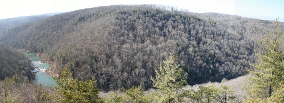 Panoramic view over river winding through hills covered by bare trees.
