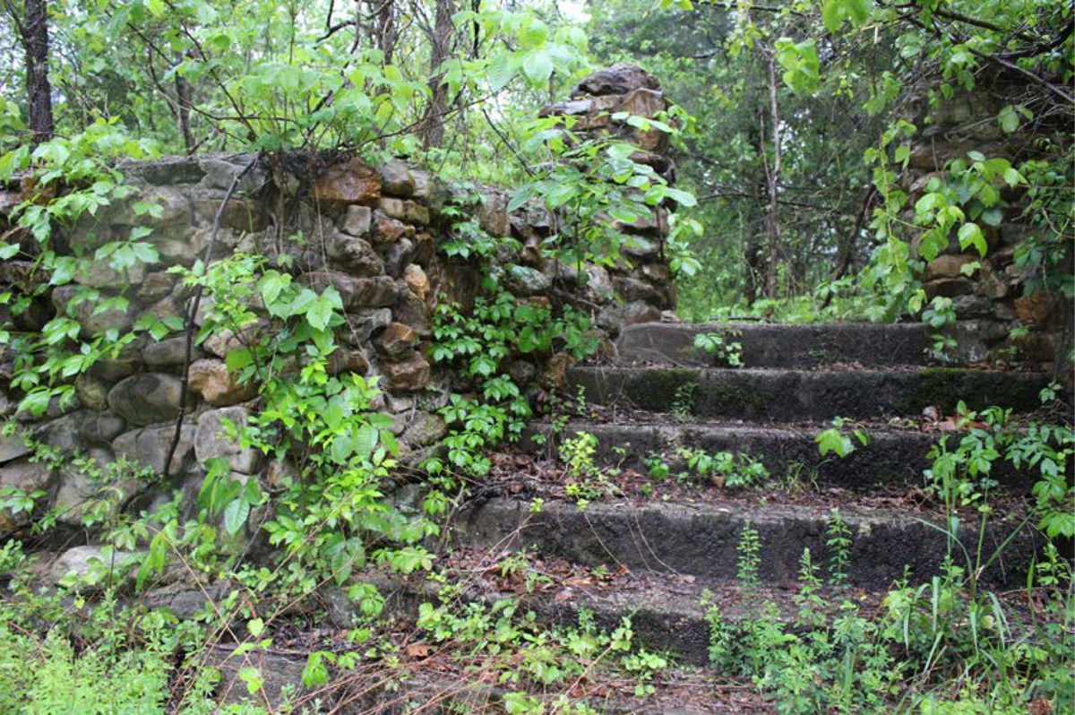 Vegetation grows in the cobblestone wall, columns, and concrete stairs.
