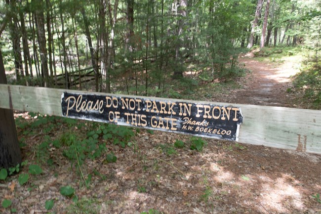 Boekeloo Barrier Fence A sign on a wooden gate across a trail in the woods says "Please do not park in front of this gate. Thanks, M.W. Boekeloo"