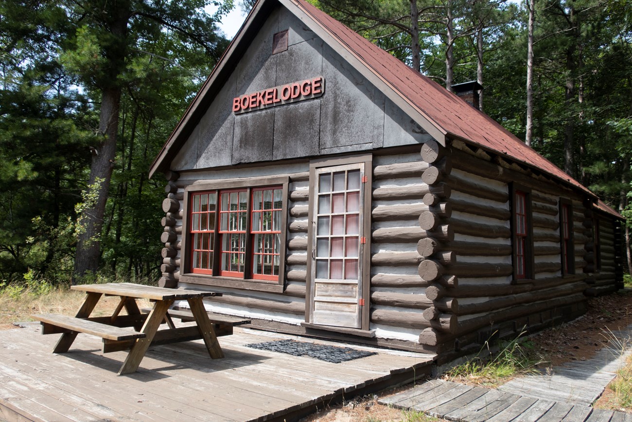 Boekeloo Cabin A log cabin with a pitched roof and the word "Boekelodge" on the front, with a picnic table on a platform in front