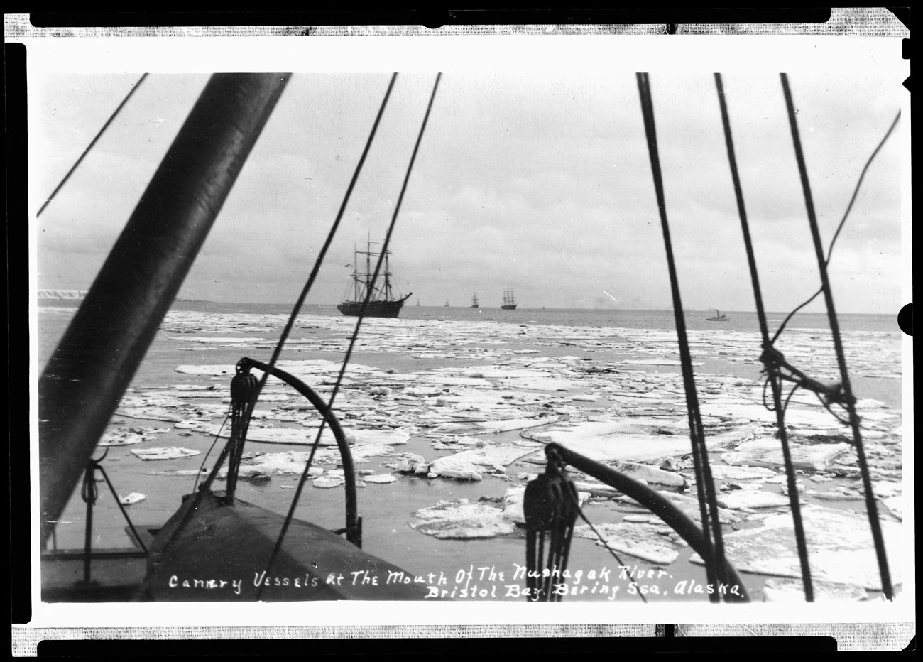 Ships with tall masts sail between chunks of ice floating on the surface of water, black and white photo