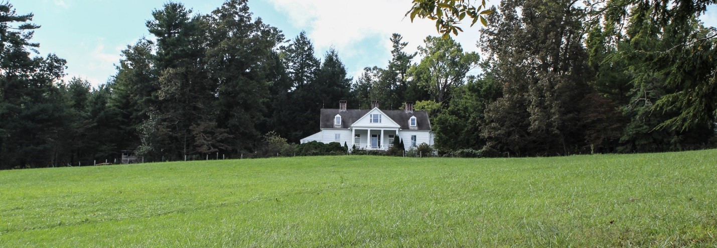 A grassy expanse in front of a white house with columns, framed by dense green vegetation