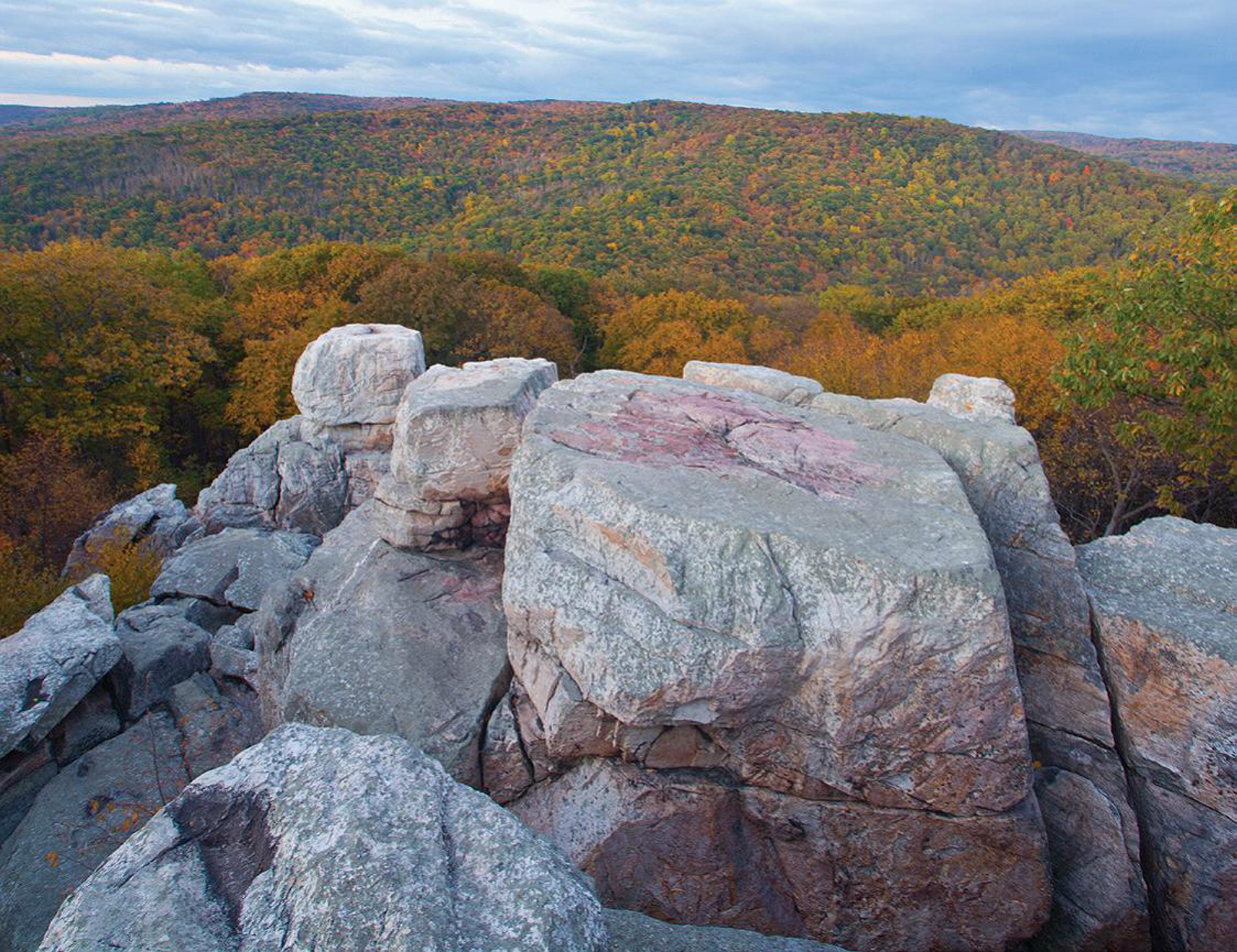 Leafy hills with autumn colors extend in the distance beyond a rocky outcropping